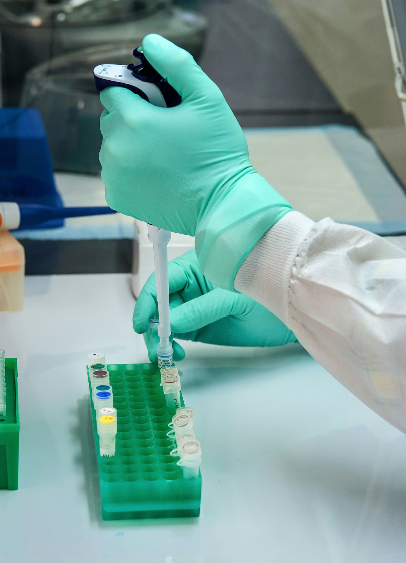 a gloved hand pipetting into a rack of tubes in a laboratory