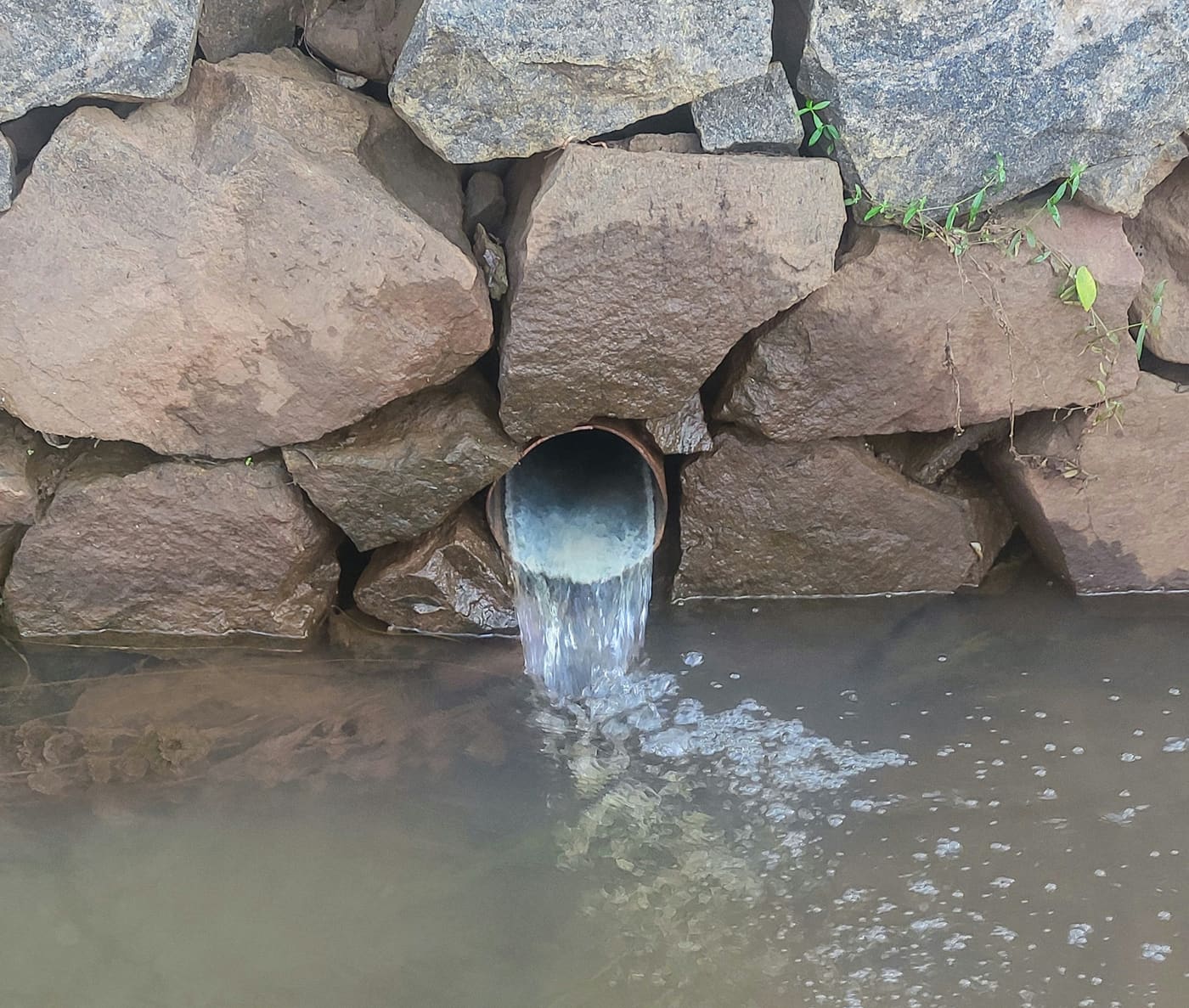 an outfall pipe in a stone wall discharging into a river